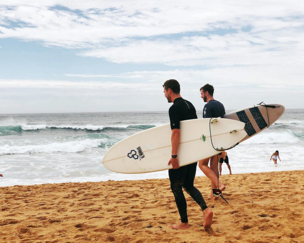 Dois surfistas caminhando na praia com uma pranchinha shortboard, prontos para o mar