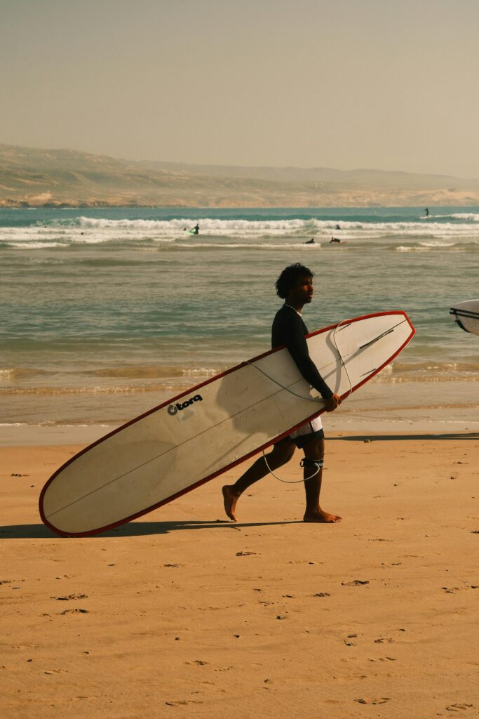 Surfista iniciante caminhando na praia com um longboard, prancha ideal para comecar